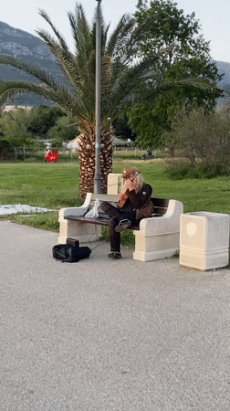 Street musician performs lute on park bench in Bar