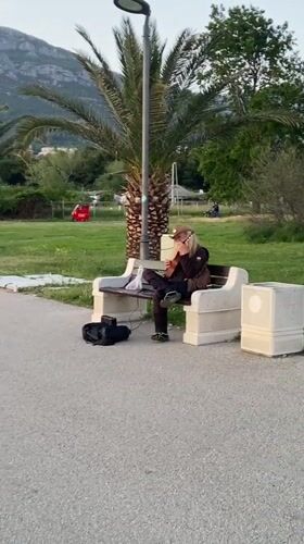 Street musician performs lute on park bench in Bar