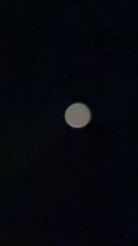 A video shows a blurry, pale disc in the center of a dark background. The disc appears to be glowing faintly and has a soft, diffused edge. The background is uniformly dark, suggesting a night sky. There are no other discernible objects or features in the video. The disc remains in the same position throughout the brief recording.