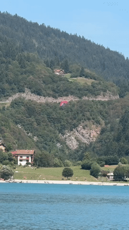 Pink paraglider over a turquoise Italian Alpine lake