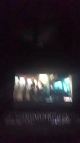 The video shows a laptop screen displaying a scene from a film or television show. The video is taken in a dark room, with only the laptop screen illuminated. The on-screen scene appears to show a physical altercation between two people inside what looks like a train car or a similar enclosed space. The lighting within the on-screen scene is bright, creating contrast with the surrounding darkness. The rest of the laptop, including the keyboard, is visible. The ceiling, obscured by darkness, shows a hint of what may be a fan.