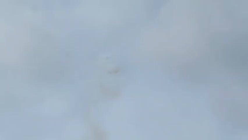 The video shows a faint object in a cloudy sky, emitting a trail of smoke. The object appears to be a small aircraft, possibly a jet, in the process of a maneuver or experiencing some kind of incident. The smoke is a light brown or tan color and trails behind the object. The overall scene is hazy due to the clouds, making it difficult to discern fine details.