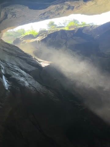 This media file captures a view looking down into a gorge, likely in Mürren, Switzerland. The scene is dominated by sheer, rocky cliffs that form a narrow opening above, through which sunlight streams down. This light illuminates a significant amount of mist or spray, creating a hazy, ethereal atmosphere.

The primary subject is the natural landscape itself, specifically the dramatic rock formations and the water that is creating the mist. It appears to be a waterfall or a fast-flowing stream within the gorge, as the mist is dense and widespread. The sunlight hitting the water particles refracts, creating a visible rainbow in the lower right portion of the frame, a beautiful and fleeting phenomenon.

The time of day is suggested by the bright sunlight piercing through the opening, indicating it is likely daytime, perhaps late morning or early afternoon. The weather appears to be clear enough for the sun to shine, but the presence of the mist suggests humidity or a significant source of water. The steep, wet-looking rock faces on the left side of the gorge further support the idea of a water feature.

The emotion evoked is one of awe and natural beauty. The grandeur of the gorge, the play of light and mist, and the presence of the rainbow all contribute to a sense of wonder. There is a feeling of being immersed in a powerful and majestic natural environment.

No people or objects are explicitly visible. There is no visible text in the media file. The location context of Mürren, Switzerland, suggests the possibility of alpine scenery, which aligns with the rugged, mountainous terrain depicted.
