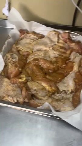 The video shows a person preparing food in a kitchen setting, likely a commercial one. The initial shot focuses on a metal tray lined with parchment paper, filled with raw chicken pieces that appear to be marinated. The chicken is a mix of cuts, including what look like thighs and smaller pieces. The marinade has a golden-brown hue and is seasoned with visible spices.

The scene then shifts to a stainless steel countertop. A large white bottle, possibly containing a liquid ingredient like oil or sauce, is visible, along with other items that are out of focus.

Further cuts show a stainless steel pot on an induction cooktop, with steam rising from within, indicating something is boiling or simmering. The cooktop has a digital display showing "08" and a dial for temperature control. A prominent logo with Cyrillic text is visible on the front of the cooktop, and it reads "Мастерский вкус" which translates to "Masterful taste".

There are brief, blurred shots of the kitchen floor and a person walking. The overall impression is a busy kitchen environment where food preparation is underway. The time of day is not explicitly indicated, but the lighting suggests it could be daytime. The location is identified as Lvovskoye, Russia.
