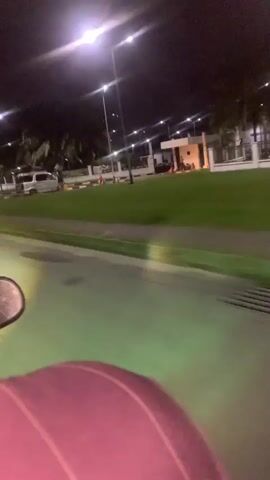 The video begins with a slightly blurry, nighttime shot of a street. In the foreground, a pink object is visible, possibly part of a vehicle or a piece of equipment. The street appears to be paved, and there is a grassy area to the right, illuminated by streetlights. In the background, there are some buildings and trees, also lit by streetlights. The camera is moving, suggesting that the video was taken from a moving vehicle or while someone was walking.

The video then transitions to a completely blurred, solid pink image, with no discernible details.

Finally, the video ends with a completely blurred, solid red image, also with no discernible details. The transition between the pink and red screens is abrupt.