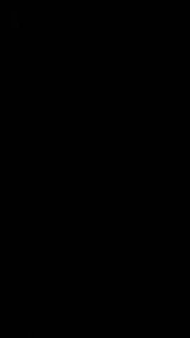 The video features a woman in a very dark, likely indoor setting. Her face is the only part of her visible, illuminated solely by the light emanating from a smartphone she is holding. The scene is predominantly black, with the phone's glow casting light on her face from below. The woman appears to be looking directly at the phone, possibly recording herself or viewing content. Her expression is neutral and focused, without strong emotions. The lack of ambient light indicates it is either nighttime or she is in a poorly lit room. There are no specific objects or location cues visible in the video to suggest Winnipeg, Canada, beyond the provided context. No visible text appears in the frame.