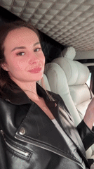 Woman with pink item makes peace sign in vehicle