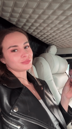 Woman with pink item makes peace sign in vehicle