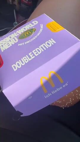 A person holds a McDonald's burger box with "ich liebe es" printed on it, then opens the box to reveal a burger with sesame seed bun, two beef patties, and melted cheese. The person's hand is shown adjusting the burger inside the box.