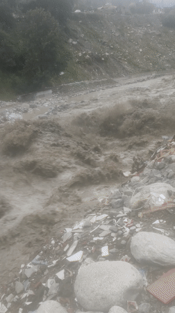 Sediment-heavy floodwater churns through debris-covered Manali terrain