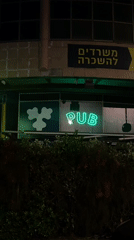 Neon pub sign cycles colors on Tel Aviv building