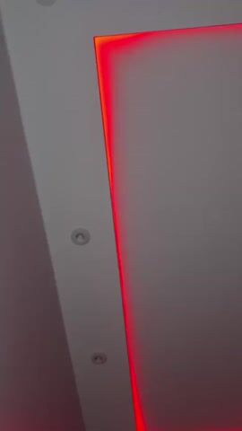 This video shows a view of a ceiling with recessed lights and accent lighting. The accent lighting is red and outlines a rectangular area of the ceiling. The camera is angled upwards, showing a portion of a wall on the left side of the frame.