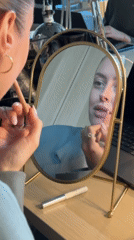 Woman applies lip makeup at desk mirror in London