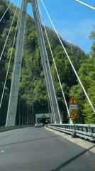White car crosses suspension bridge toward tunnel in Kepsha