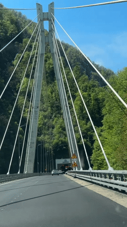 White car crosses suspension bridge toward tunnel in Kepsha