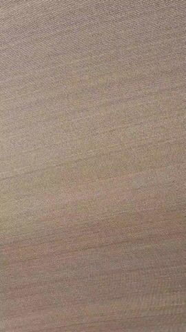 The video shows a close-up, static shot of textured fabric, likely clothing or upholstery, with a beige to light brown color. The weave of the fabric is visible, with a slight fold or drape at the bottom creating a subtle shadow. The lighting is even, highlighting the texture of the material.