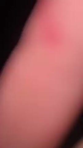 A young woman with a fair complexion is shown in the video. She is wearing a green ribbed tank top and a heart-shaped necklace. Her hair is pulled back in a bun. She has small earrings in her ears. She is smoking a hookah. The background is dark, but there are string lights visible. The video appears to be taken outdoors at night. A small child is heard calling out in Russian.