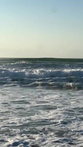 The video shows a view of the ocean with waves. The sky is clear and blue. The waves are breaking and creating white foam. The water is a dark blue color.