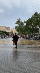 Couple spotted in rainy Barcelona square during afternoon shower