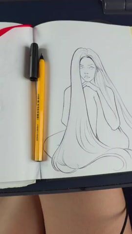 The video begins with a close-up shot of a sketchbook open to a drawing of a woman with long, flowing hair. A yellow marker and a black pen are visible on the left side of the sketchbook. The camera then pans to the right, revealing the interior of a train. The seats are visible, along with the window. The view from the window shows a blur of a golden field under a bright blue sky with fluffy white clouds. The camera continues to pan, showing more of the field and sky as the train moves.