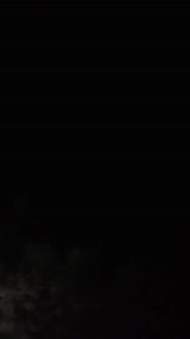 The video is very dark and shows a brief flash of purple light in the sky, suggesting lightning. It appears to be nighttime and there are some dark shapes that could be trees or land in the foreground. The image is grainy and there is a lot of blackness throughout the short clip.