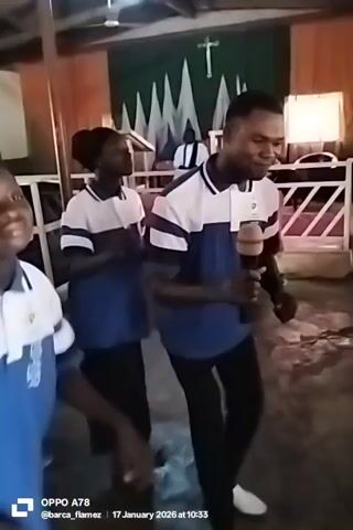 The video shows a group of people, mostly children, indoors. They are wearing blue and white uniforms. A man is holding a microphone and appears to be speaking or singing, and the group seems to be dancing or moving to music. The room has a simple interior with a wooden ceiling and some posters on the walls. The lighting is somewhat dim. The camera moves a bit erratically. An Oppo A78 watermark is present at the bottom left corner of the screen, along with a date and time stamp: 17 January 2026 at 10:33.