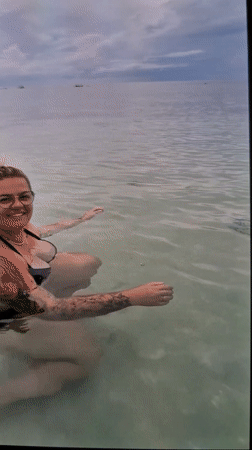 Person with tattoos stands in calm water with fish