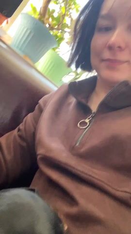 The video shows a close-up shot of a black and brown dachshund lying on a burgundy or dark brown surface, possibly a couch or blanket. The dog has its head turned slightly towards the camera, revealing one eye. The video appears to be shot at a close range, with the dog's face filling a significant portion of the frame. An arm wearing a brown sleeve is partially visible. The overall lighting appears to be soft and diffused. There is audio of what sounds like a dog panting.