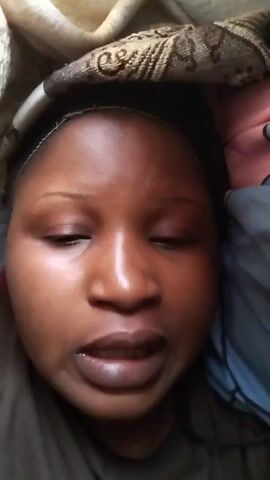 A person with brown skin and dark hair is lying down, looking into the camera. The person is wearing a dark shirt. A white and brown patterned fabric is draped over the top of the person's head.  The person appears to be in a bed, as there is a blue fabric next to them. The person says "It's weekend. I just came home today. Happy weekend."