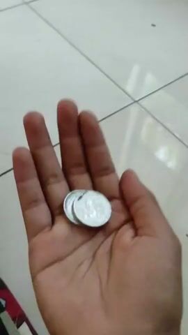 A hand holds two coins. The coins are flipped in the air and caught by the hand. The background is a tiled floor.