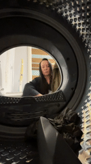 Woman loads olive towel into washing machine in Chaikovsky
