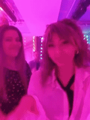 Two women dance at party under pink lights