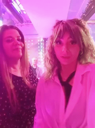 Two women dance at party under pink lights