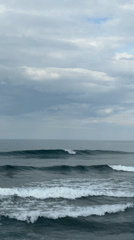 Surfers ride waves off Mengwi coast under cloudy skies