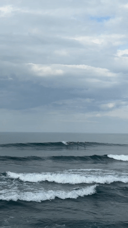Surfers ride waves off Mengwi coast under cloudy skies