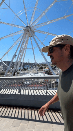 Tourist strolls Barcelona waterfront near Ferris wheel and W Hotel