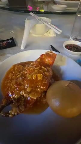 The video shows a woman at an outdoor restaurant. The video starts with a close-up of a plate of chili crab with a fried mantou bun. The camera then quickly pans to the woman, who is seated at the table, and she yells. The camera quickly pans back to the plate of food. The restaurant is lit with string lights.