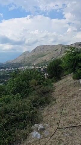 This media file is a video showcasing a scenic view of a coastal landscape in Plat, Croatia. The scene is dominated by a large body of water, likely the Adriatic Sea, with a town nestled along the coastline in the distance. Mountains rise behind the town, their slopes covered in sparse vegetation. The foreground is filled with lush green bushes and trees, suggesting a natural, untamed environment.

The time of day appears to be late afternoon or early evening, as indicated by the soft lighting and the presence of scattered clouds in a bright blue sky. The weather seems pleasant, with a mix of sunshine and light cloud cover. The video captures a peaceful and serene atmosphere, with the calm waters reflecting the sky and the distant mountains.

A notable feature is a small harbor with several boats docked. This suggests a connection to maritime activities and a potential tourist destination. The presence of the town and harbor implies human habitation and a community that thrives on the coast.

There is no visible text within the media file. The overall emotion conveyed is one of tranquility and natural beauty, inviting the viewer to appreciate the stunning landscape.