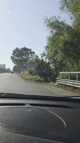 A video shows a view from the dashboard of a car. The car is driving down a paved road. On the right side of the road is a sign that reads "SALINO". Further down the road, there are buildings and trees. The sun is shining and the sky is blue. The video appears to be taken on a clear day.