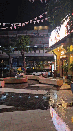 Rainy night reflections across a Bangkok plaza and walkway