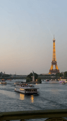 Eiffel Tower glowing at dusk as tour boats cruise the Seine