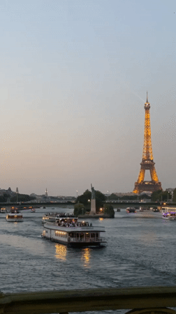 Eiffel Tower glowing at dusk as tour boats cruise the Seine