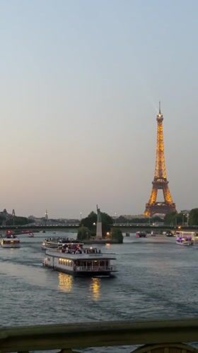 Eiffel Tower glowing at dusk as tour boats cruise the Seine