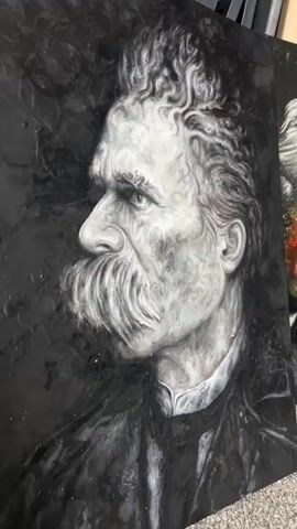 The video features two distinct artistic portraits, likely oil or acrylic paintings on canvas, positioned next to each other.

The first painting, initially prominent in the frame, is a monochrome portrait of Friedrich Nietzsche, depicted in profile, facing left. The artwork uses a grayscale palette with strong contrasts, highlighting his distinctive bushy mustache and curly hair. The background is dark and textured, adding depth to the somber portrayal.

As the camera pans to the right, a second painting becomes fully visible. This portrait, rendered in vibrant colors, appears to be of Carl Jung. His face is painted with warm, fiery hues of red, orange, and yellow, contrasting with the dark background and his white, wispy hair. He is shown wearing glasses and smoking a pipe, with a contemplative expression.

Both paintings are rectangular and appear to be propped up, possibly on a floor or low surface, in what seems to be an indoor setting, perhaps an art studio or gallery. The camera smoothly transitions between showcasing each artwork. No text is visible on the paintings or in the immediate surroundings.