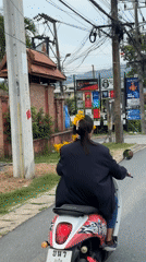 Woman rides flower-adorned scooter through Chalong, Thailand