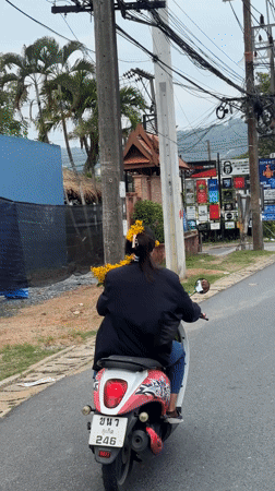 Woman rides flower-adorned scooter through Chalong, Thailand