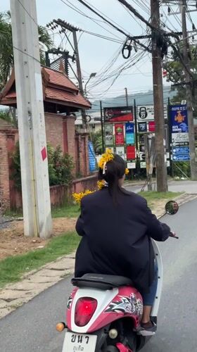 Woman rides flower-adorned scooter through Chalong, Thailand