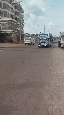 The video depicts a street scene in what appears to be an urban area. A building is visible in the background, along with other vehicles on the road. The main subject is a minibus with distinctive blue and white paint, decorated with cartoonish images including a character wearing a green hat and sunglasses. The words "VIP" and "SOURCE" are also prominent on the front of the bus. The camera focuses on the bus's exterior, showcasing the detailed paint job. Someone wearing yellow shoes and pink pants briefly appears in the frame, walking past the bus. The sound of a car horn can be heard.