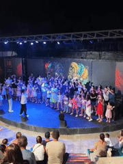 Kids and adults perform on a blue-lit stage in Kuşadası