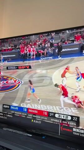The video shows a television screen displaying a WNBA basketball game between the Dallas Wings and the Indiana Fever. The score is Dallas 18, Indiana 16 in the first quarter with 3 minutes and 7 seconds remaining. The game is broadcast on ESPN. Several players are visible on the court in their respective team uniforms, one blue and white and the other red and white. The court is painted red and white in the center. There are spectators in the background. The bottom of the screen displays the game information, including last season records, tip-off time, and odds for the Thunder vs. Lakers game. The television is a Sony and is sitting on a black stand.